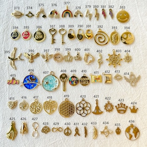 May include: A collection of gold-colored charms in various shapes, including a smiley face, lightning bolts, keys, crowns, and a world map. Some charms feature enamel details in colors like blue, red, and green. These charms are ideal for jewelry making.