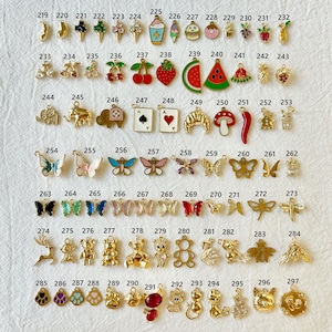 May include: A collection of small, gold-toned charms with various designs, including butterflies, fruits, animals, and playing card suits. Some charms feature colorful enamel details, perfect for jewelry making or crafting projects.