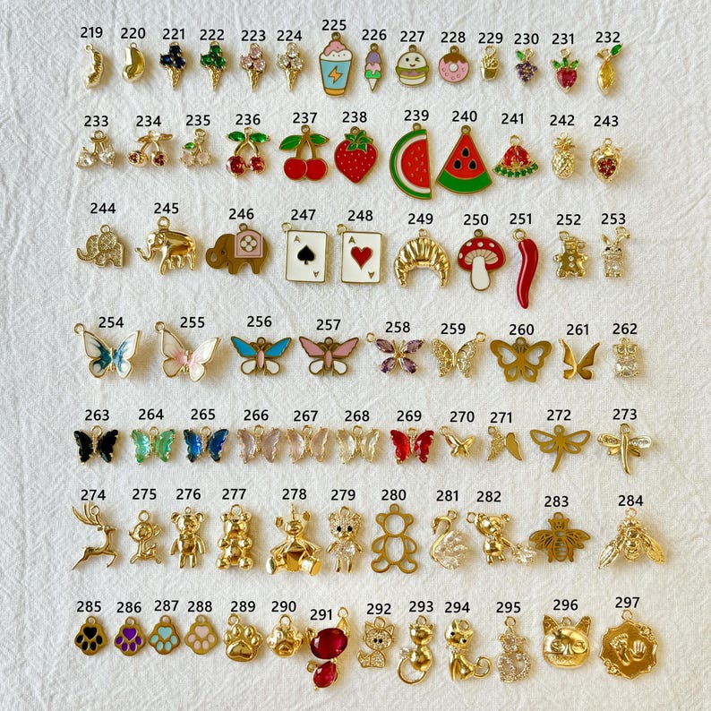 May include: A collection of small, gold-toned charms with various designs, including butterflies, fruits, animals, and playing card suits. Some charms feature colorful enamel details, perfect for jewelry making or crafting projects.