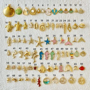 May include: A collection of gold-toned and colorful ocean-themed charms, including shells, starfish, seahorses, and fish. These small pendants are designed for jewelry making, with a variety of shapes and sizes.