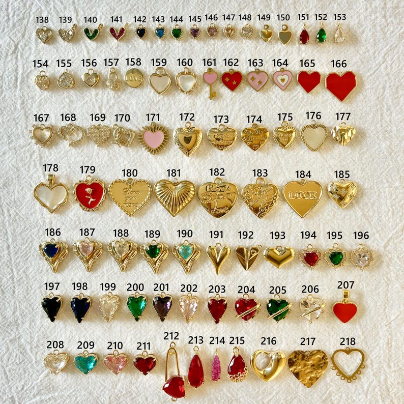 May include: A collection of gold-toned and colorful charms in various shapes, including hearts, teardrops, and geometric designs. Some charms feature gemstones, enamel, or text. The charms are arranged on a white surface.