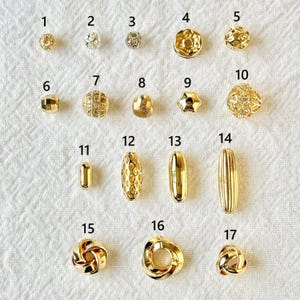 Op de afbeelding: Een verzameling van zeventien goudkleurige kralen in verschillende vormen en ontwerpen. De kralen omvatten ronde, facetgeslepen en langwerpige stijlen, geschikt voor het maken van sieraden of knutselprojecten. De kralen worden gepresenteerd op een witte, getextureerde ondergrond.