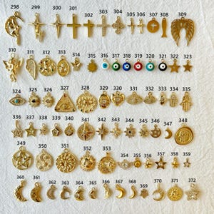 May include: A collection of gold-colored charms in various shapes, including crosses, stars, moons, and angel wings. The charms are designed for jewelry making or crafting, with a variety of celestial and religious symbols.