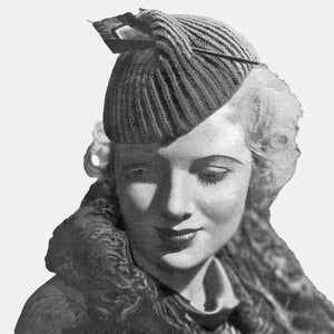 May include: A black and white photograph of a woman wearing a knitted hat with a decorative detail on top. She is wearing a fur collar and looking down.