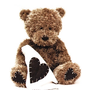 May include: A brown teddy bear holding a white fabric heart-shaped pillow. The pillow has a black heart sewn onto it.