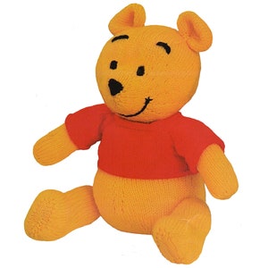 May include: A knitted plush toy of a bear in a seated position. The bear is primarily yellow with a red shirt. It has black eyes and a smiling mouth. The toy is made of soft yarn and has a classic, friendly appearance.