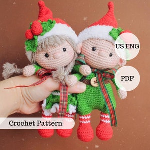 May include: Crochet pattern for two elf dolls, one with a green dress and one with a red dress. The dolls are holding hands and have red and white striped socks. The pattern is available in US English and PDF format.