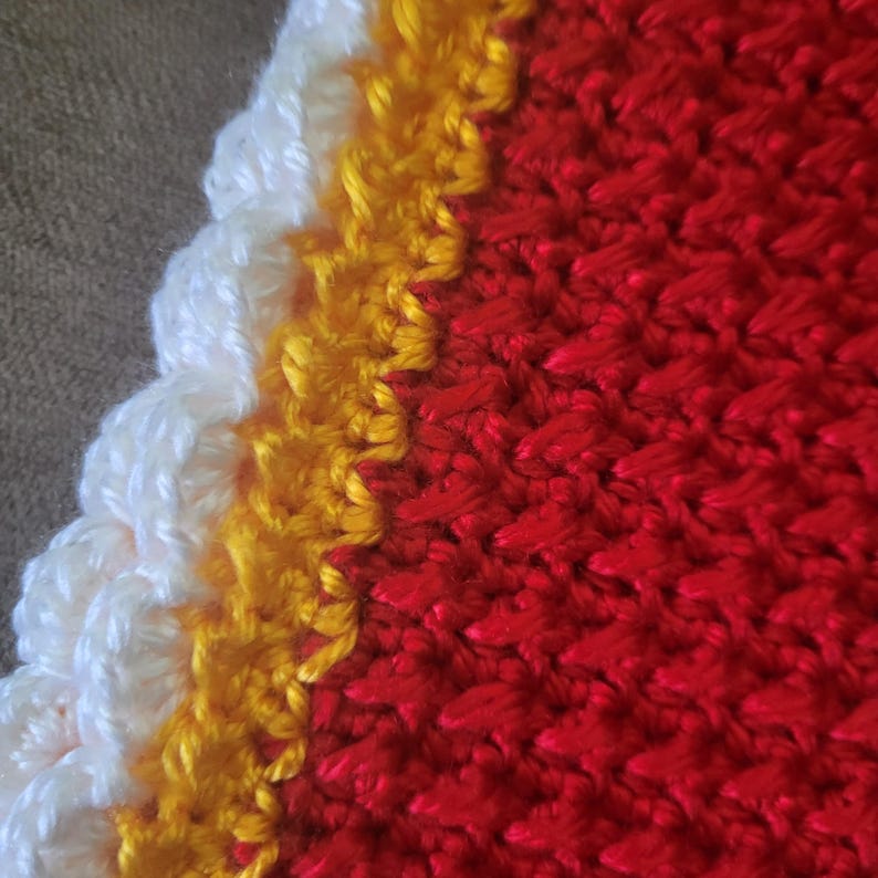 May include: Close-up of a crocheted fabric with a white, yellow, and red color scheme. The fabric has a textured, woven appearance.