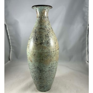 Puede incluir: Un jarrón alto y esbelto con una superficie moteada y jaspeada en tonos verdes, beige y negro. El jarrón tiene un cuello estrecho y un borde marrón oscuro. La forma general es alargada y ligeramente bulbosa, adecuado para la decoración del hogar.