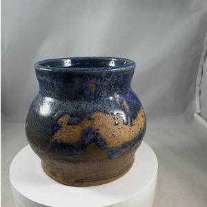 May include: A handmade ceramic vase with a rounded body and a wide opening. The vase features a dark blue glaze on the top half, transitioning to a tan-colored base. The vase is approximately 6 inches tall.