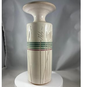 Puede incluir: Un jarrón de cerámica de color crema, alto, con una parte superior ancha y plana y un cuerpo cilíndrico. El cuerpo presenta líneas verticales finas de color beige y rayas horizontales verdes y granates. El jarrón es probablemente para fines decorativos.