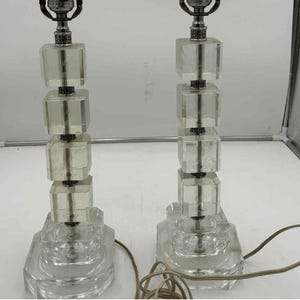 Könnte beinhalten: Zwei Tischlampen aus klarem Glas mit einem Design aus gestapelten Würfeln. Jede Lampe hat einen silberfarbenen Metallsockel und einen klaren, facettierten Schirm. Die Lampen sind durch braune Kabel verbunden.