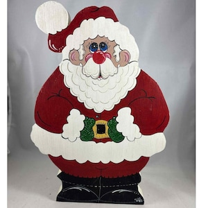 May include: Wooden Santa Claus figure, painted in red, white, black, and green. The figure has a round white beard, a red nose, and blue eyes. The figure is wearing a red suit with a white trim and a black belt with a gold buckle. A white ball is on top of the hat.