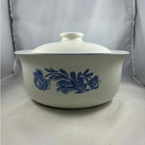 Może przedstawiać: Kremowa ceramiczna forma do zapiekania z pokrywką. Naczynie posiada niebieski kwiatowy wzór i niebieską obwódkę wokół krawędzi. Pokrywka jest biała z małym uchwytem.