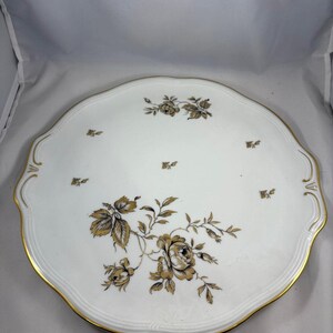 May include: A white porcelain serving platter with a gold rim and a black and gold floral design.