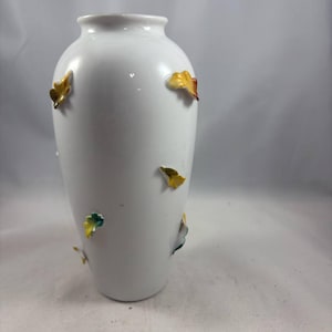 May include: White ceramic vase with a decorative design of yellow, green, and orange leaves.
