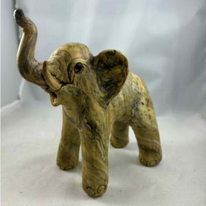 May include: A decorative elephant figurine with a trunk raised in the air. The elephant is tan with dark brown marbling throughout. The figurine has large ears and small black eyes. The elephant is standing on four legs.
