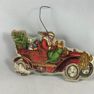 Adorno navideño antiguo de Papá Noel conduciendo un coche vintage troquelado de cartón aglomerado