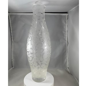 Puede incluir: Un jarrón alto de vidrio transparente con un patrón de remolino esmerilado. El jarrón tiene un cuerpo ancho y redondeado que se estrecha hacia la parte superior y se asienta sobre una base circular. El diseño grabado añade un elemento decorativo.