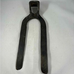 Op de afbeelding: Een vintage, donker metalen tuinhark met een U-vormig ontwerp. De hark heeft een rechthoekige aansluiting voor een handvat en twee lange, platte bladen. Het metaal heeft een verweerde uitstraling, wat duidt op leeftijd en gebruik. Deze tool is ontworpen voor het bewerken van de grond.