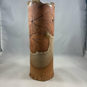 May include: A ceramic vase with a brown and white glaze. The vase has a unique, irregular shape and is decorated with a leaf pattern.