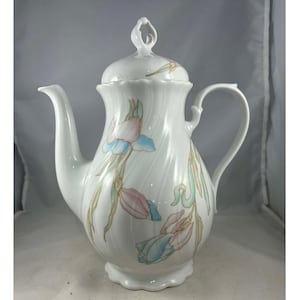 May include: White porcelain coffee pot with a lid and handle, decorated with pastel-colored iris flowers. The pot has a curved spout and a decorative handle. The iris flowers are in shades of pink, blue, and yellow.