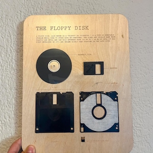 May include: A wooden plaque with the text "The Floppy Disk" and a description of the history of floppy disks. The plaque features images of different sizes of floppy disks, including a 5.25-inch floppy disk, a 3.5-inch floppy disk, and a magnetic disk.
