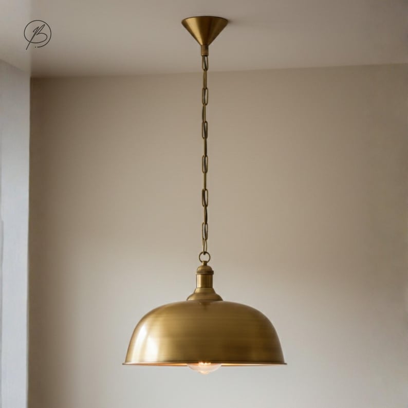 May include: A brass pendant light with a domed shade, suspended from a chain and a conical ceiling fitting. The light fixture has a vintage or industrial style, suitable for interior lighting, with a warm, metallic finish.