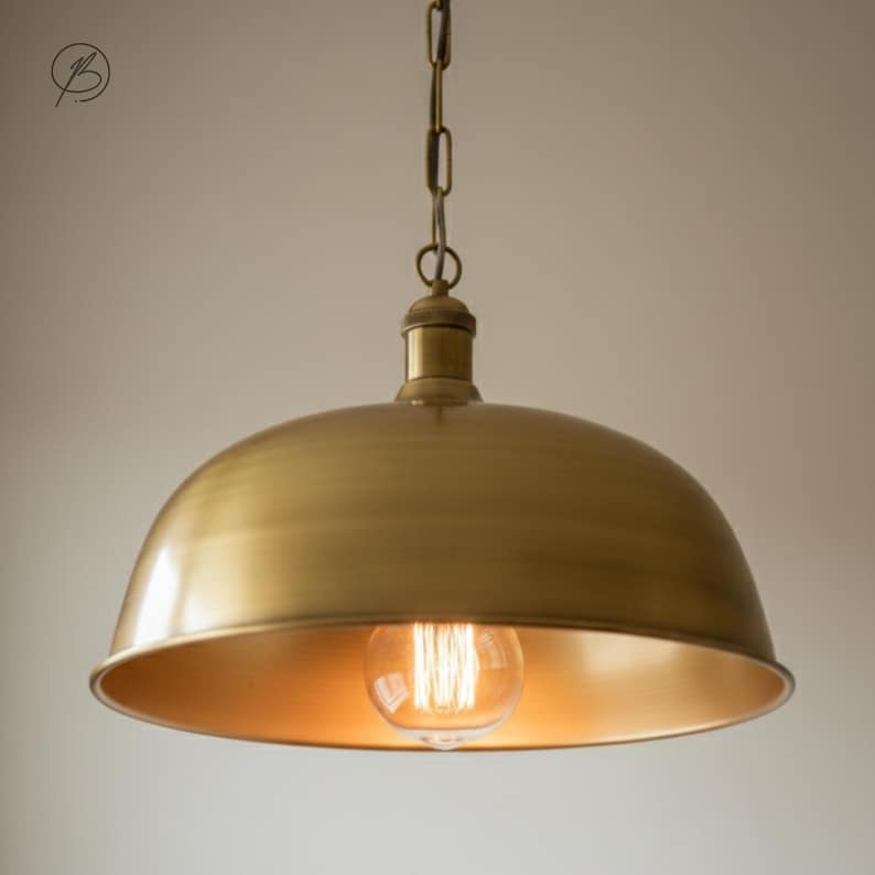 May include: A brass-coloured pendant light fitting with a domed shade and a visible Edison-style light bulb. The fitting hangs from a chain. The interior of the shade has a warm, golden hue, and the overall design is vintage-inspired.