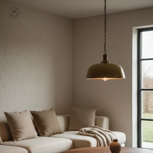 May include: A bronze pendant light suspended from a chain in a living room. The light has a rounded, dome-shaped shade and a single exposed bulb. The room features a neutral colour palette with a cream sofa, throw cushions, and a wooden coffee table.