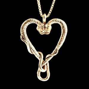 May include: A gold-toned pendant necklace featuring a snake shaped into a heart. The snake's head is visible at the top of the heart.
