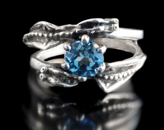 May include: A silver ring with a blue gemstone set in a twisted band. The ring is designed with a textured, organic pattern.