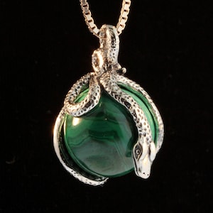 Op de afbeelding: Een zilveren ketting met een hanger met een groene malachiet steen omhuld door twee zilveren slangen.