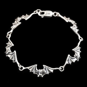 Op de afbeelding: Een zilveren armband met een herhalend patroon van vleermuisbedels. De armband is gemaakt van een delicate ketting en heeft een karabijn sluiting.