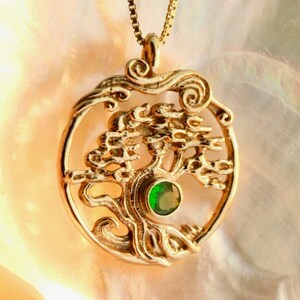 May include: Gold necklace with a tree of life pendant featuring a green gemstone. The pendant is round and has a detailed design.