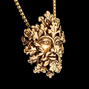 Pu&ograve; includere: Una collana d'oro con un ciondolo che presenta un designo dettagliato di Green Man. Il ciondolo &egrave; in metallo e ha un viso circondato da foglie e rami.