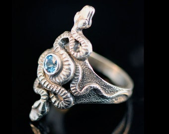 May include: A silver ring with a detailed snake design and a blue gemstone in the center.