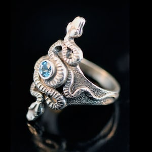 May include: A silver ring featuring a detailed snake design with a blue gemstone at its centre.