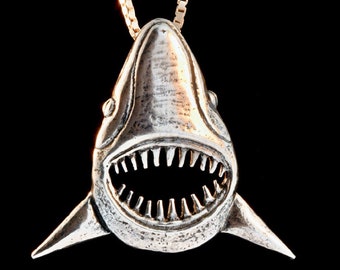May include: A silver shark pendant with a detailed open mouth and sharp teeth, hanging from a gold chain.
