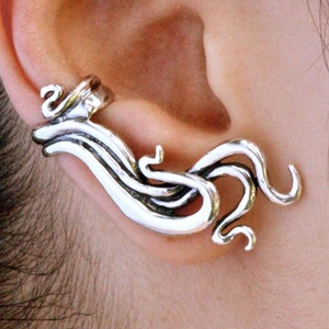 May include: Silver ear cuff with a wave-like design. The cuff is made of metal and has a smooth finish.