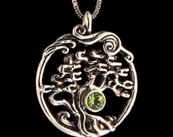 May include: A silver tree of life pendant necklace with a green gemstone in the center. The pendant is round and features a detailed design of a tree with branches and leaves.