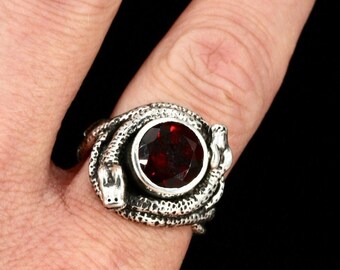 May include: A silver ring featuring a coiled snake design with a red gemstone in the center.