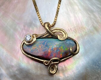May include: A gold pendant necklace with a large, oval-shaped opal gemstone set in a gold filigree design. A small, round diamond is set in the gold filigree above the opal.