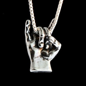 May include: A silver necklace with a pendant of two hands clasped together. The hands are detailed and realistic, and the necklace is made of a delicate chain.
