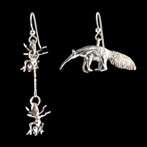 May include: A pair of silver earrings, one featuring an ant and the other an anteater.