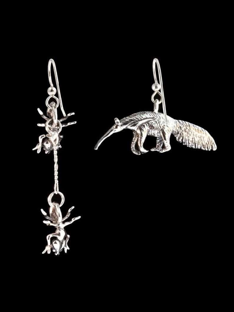 May include: A pair of silver earrings, one featuring an ant and the other an anteater.