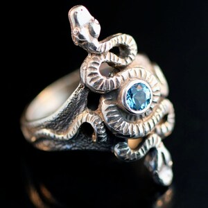 May include: A silver ring featuring a detailed snake design with a blue gemstone at its centre.