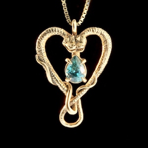 May include: A gold heart-shaped pendant necklace with two intertwined snakes and a teardrop-shaped blue gemstone in the centre.