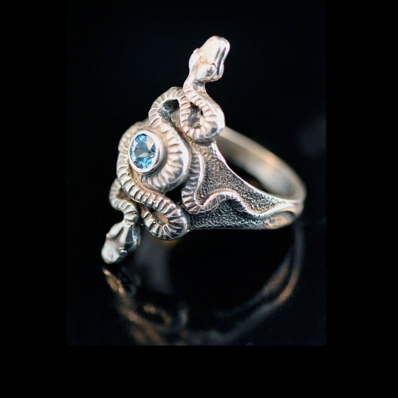 May include: A silver ring featuring a detailed snake design with a blue gemstone at its centre.