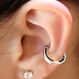 May include: A close-up of a person's ear with a silver horseshoe hoop earring and a small clear gemstone stud earring.